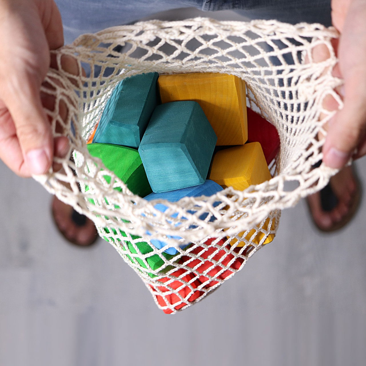 a person holding a string bag full of colorful blocks